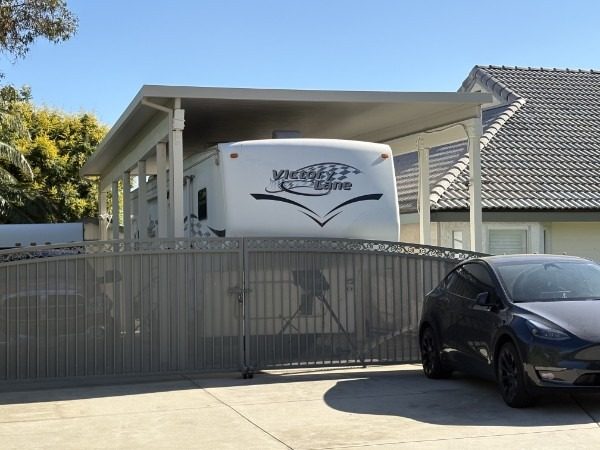 Solid aluminum RV cover alongside a residential driveway